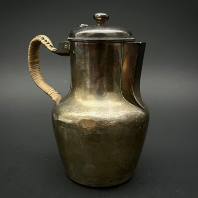 une cafetière ancienne en argent, avec une anse en forme de serpent, sur fond noir