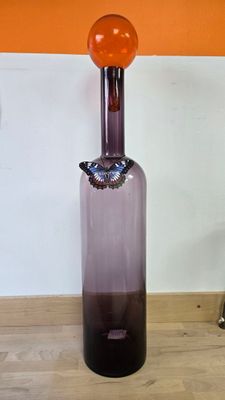 une bouteille en verre violette avec un bouchon orange posée sur une table en bois