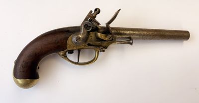 un vieux revolver en laiton avec une crosse en bois, posé sur une surface blanche
