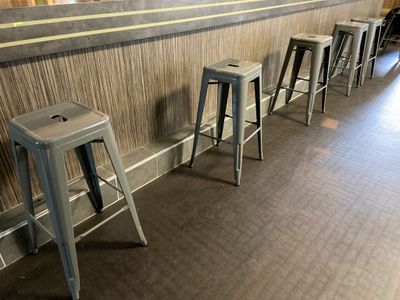 Plusieurs tabourets en métal sont alignés contre un mur dans un restaurant