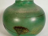 un vase vert orné d'un poisson, posé sur un fond blanc