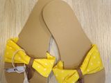 yellow flip flops with a yellow bow tied to them on a wooden floor