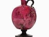 a pink vase with a black handle sitting on a stand