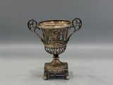an antique silver cup on a stand on a white surface