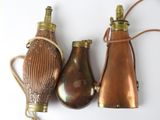 three antique brass and copper flasks on a white surface