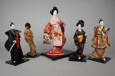 four figurines of geisha dolls are standing on a stand