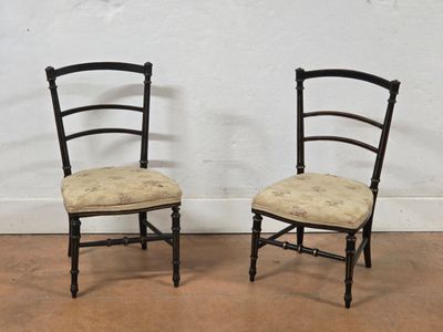 pair of black painted chairs with upholstered seats against a white wall