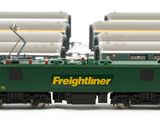 a green and yellow train on the tracks next to other trains