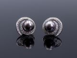 une paire de boucles d'oreilles en perles noires et diamants posées sur une surface réfléchissante