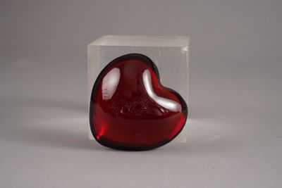 un objet en verre rouge en forme de cœur, placé dans une boîte transparente