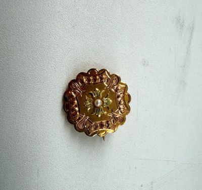 un gros plan d'une broche en forme de fleur dorée sur un mur blanc