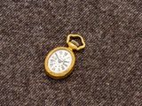 une petite montre de poche en or posée sur un tissu marron
