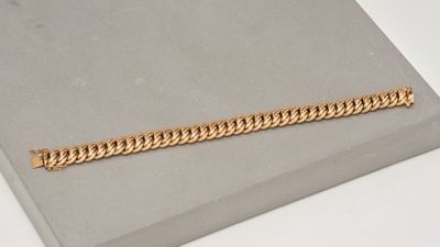 gros plan d'un bracelet en chaîne en or sur une surface blanche