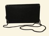 the black clutch bag has a chain around it and is on a white background