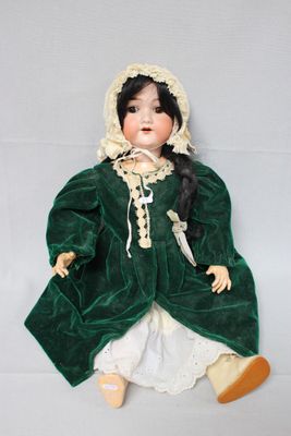 an old doll with a green dress and bonnet is laying on a white surface