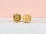 a pair of gold coin stud earrings sitting on top of a marble counter
