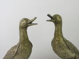 two bronze ducks standing next to each other on a table