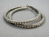 paire de boucles d'oreilles créoles argentées ornées de cristaux transparents sur un fond gris