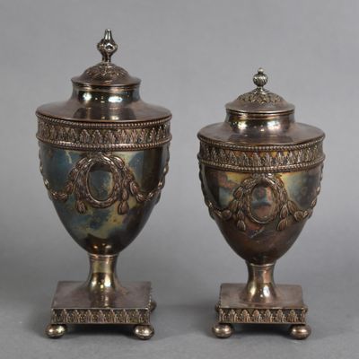 pair of antique silverplated urns on pedestals on grey background