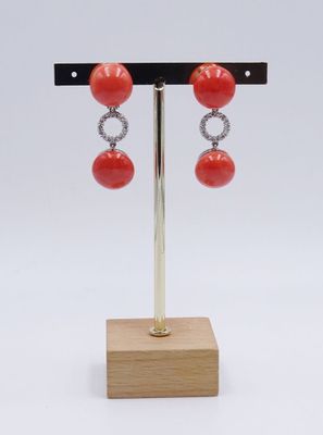 une paire de boucles d'oreilles en corail rouge et diamants, posée sur un socle en bois