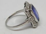 une photo d'une bague en pierre bleue et diamant posée sur une surface blanche