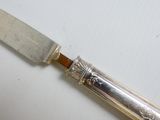 un couteau en argent avec un manche en bois posé sur une surface blanche