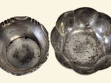 two silver dishes sitting on a white surface