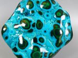 blue and green glass object with a white base on a white surface