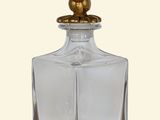 a clear glass bottle with a gold lid and a bird on the top