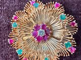 une image représentant une broche en or sertie de pierres roses, vertes et bleues