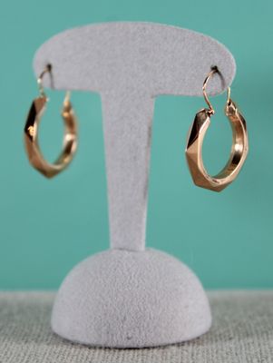 un gros plan sur une paire de boucles d'oreilles créoles en or posées sur un présentoir