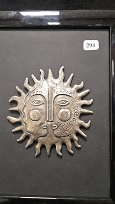 a picture of a metal sun face in a black frame