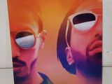 Deux hommes portant des lunettes de soleil se tiennent côte à côte devant un mur blanc.