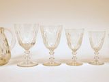 six verres à vin et un pichet sont alignés sur une surface blanche