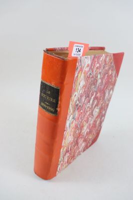 un livre rouge orné d'une étiquette noire, posé sur une surface blanche