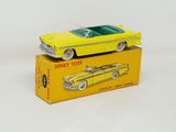 une petite voiture jaune posée sur une boîte jaune, elle-même posée sur une surface blanche