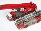 un camion de pompiers miniature et une grue miniature posés sur une surface blanche