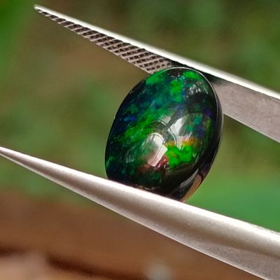 un gros plan d'une pierre verte et noire tenue par une pince