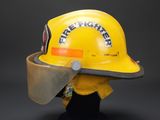 yellow firefighter helmet with protective face shield on display against a black background