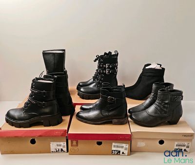 quatre paires de bottes noires sont posées sur des cartons, sur une table