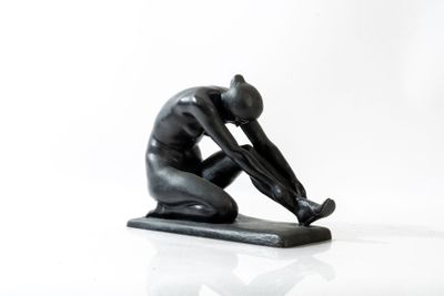 une statue noire représentant un homme à genoux sur une surface blanche