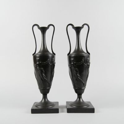 une paire de vases noirs posés sur des socles en marbre, sur fond blanc