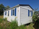 une petite maison blanche aux volets bleus, au milieu d'un champ