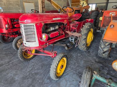 a red tractor sitting in a garage with other tractors