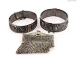 two silver bracelets and a chain purse on a white surface