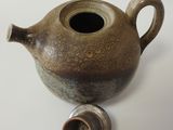 a brown tea pot with a small cup on the side