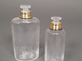 two clear glass bottles with gold lids on a gray surface