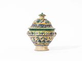 un petit vase muni d'un couvercle, posé sur une surface blanche