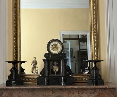 une cheminée surmontée d'une horloge, devant un miroir