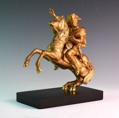 une statue en or représentant un homme à cheval, posée sur un socle noir